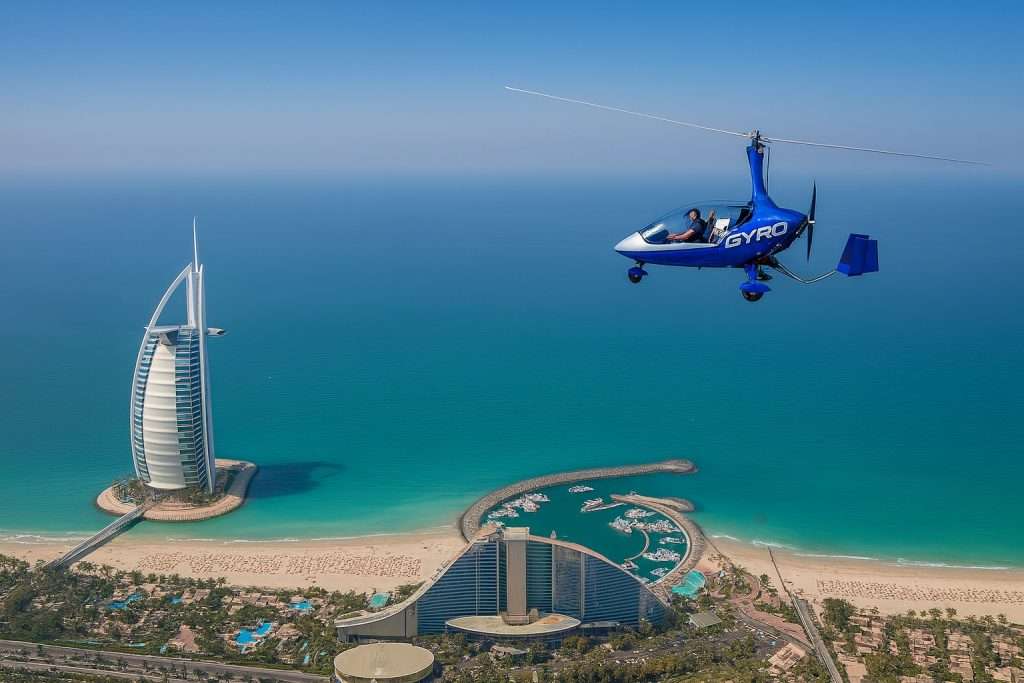 A blue gyrocopter flies over the turquoise sea near Dubai.